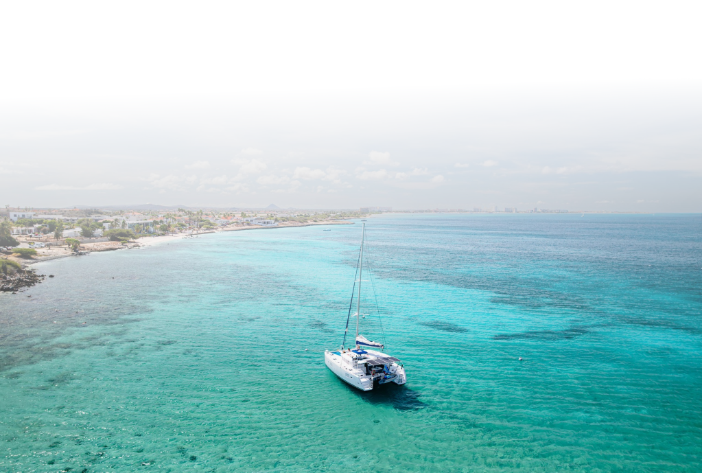 Sailboat on turquoise sea near a coastline with sparse buildings and trees.